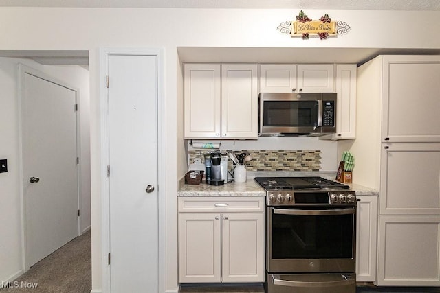 kitchen with stainless steel appliances, backsplash, white cabinets, and light stone countertops