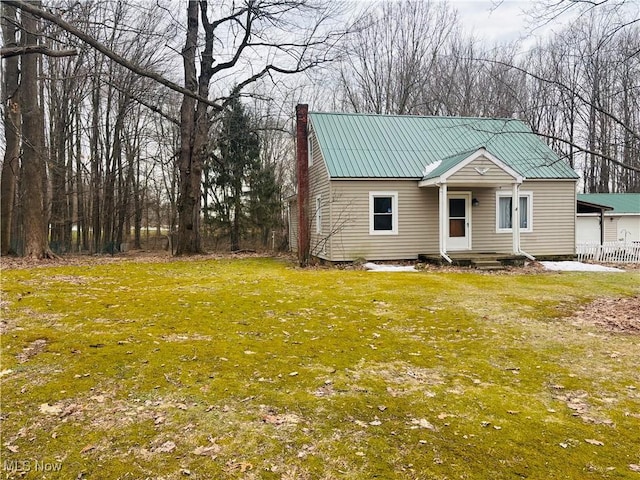 view of front facade featuring a chimney, metal roof, and a front yard