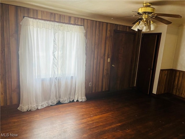 spare room with wood walls, a ceiling fan, dark wood finished floors, and a wealth of natural light