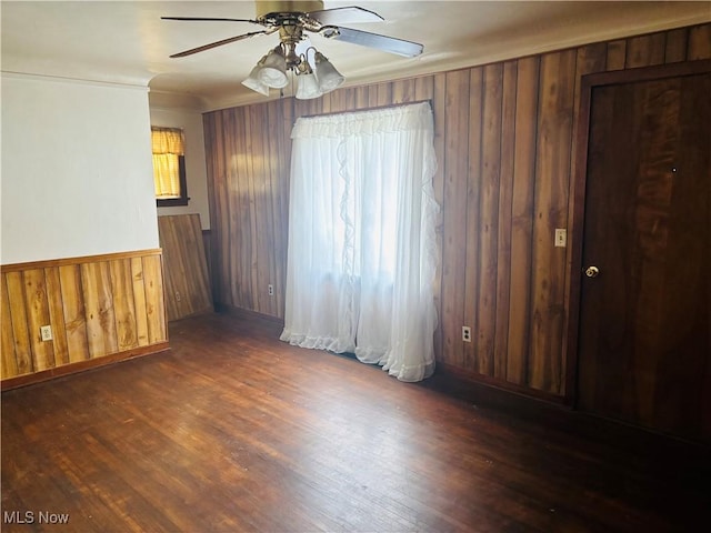 unfurnished room featuring wood walls, a ceiling fan, wood finished floors, and a wainscoted wall