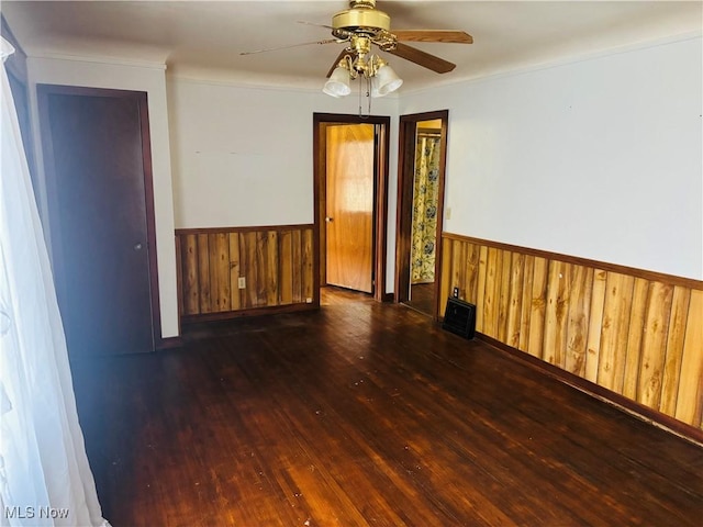 unfurnished room with a wainscoted wall, wood-type flooring, ceiling fan, ornamental molding, and wood walls