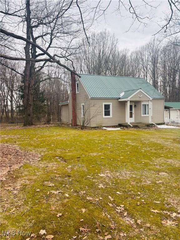 view of front of home with metal roof, a chimney, and a front lawn