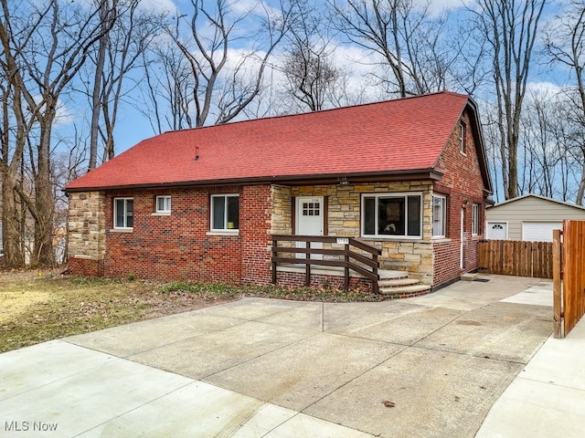 view of front of home featuring roof with shingles, a detached garage, a porch, fence, and stone siding