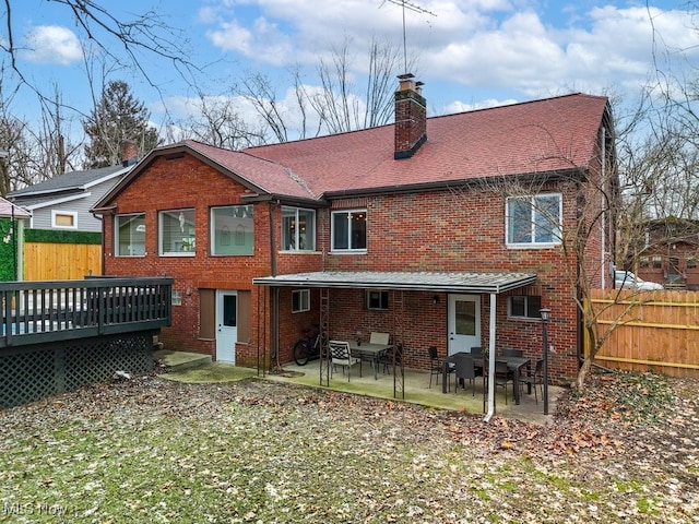 back of house with a deck, brick siding, fence, and a chimney