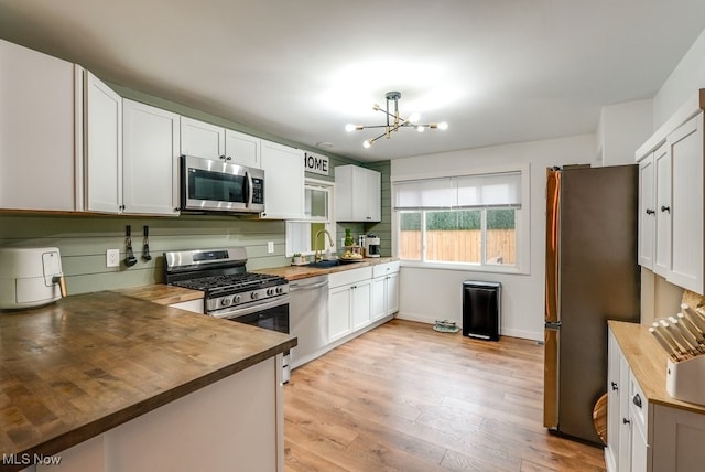 kitchen with light wood-style flooring, stainless steel appliances, a chandelier, wooden counters, and a sink