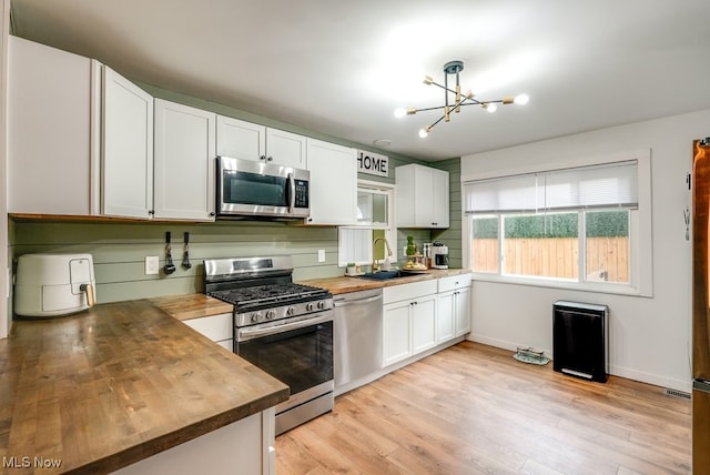 kitchen featuring appliances with stainless steel finishes, light wood-type flooring, a sink, and wood counters