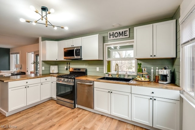 kitchen featuring butcher block counters, appliances with stainless steel finishes, a sink, light wood-type flooring, and a peninsula