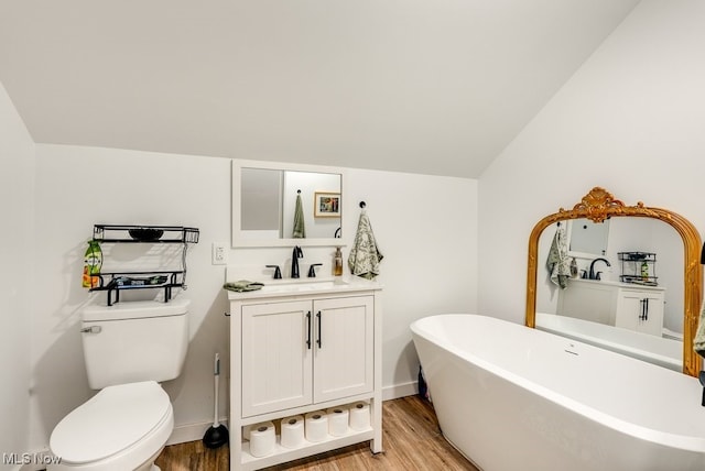 bathroom with toilet, a soaking tub, wood finished floors, vaulted ceiling, and vanity