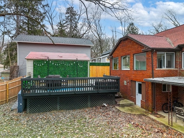 rear view of house featuring a deck, brick siding, roof with shingles, and fence