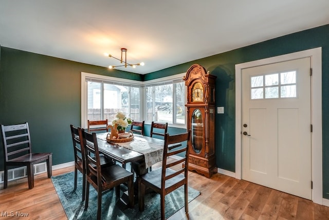 dining room with baseboards, light wood finished floors, and a notable chandelier