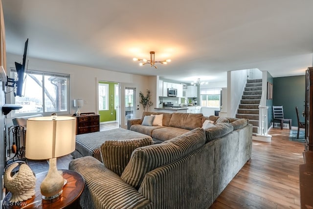 living area with stairs, wood finished floors, baseboards, and an inviting chandelier