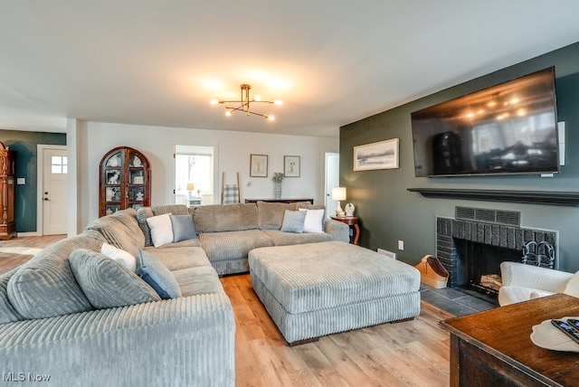 living area with light wood finished floors, a brick fireplace, and an inviting chandelier