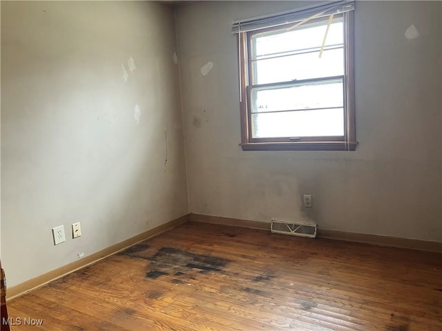 empty room with wood finished floors, visible vents, and baseboards