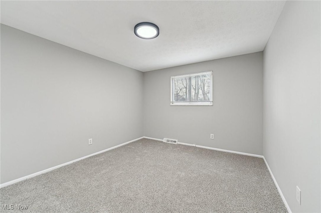 empty room with carpet floors, visible vents, and baseboards