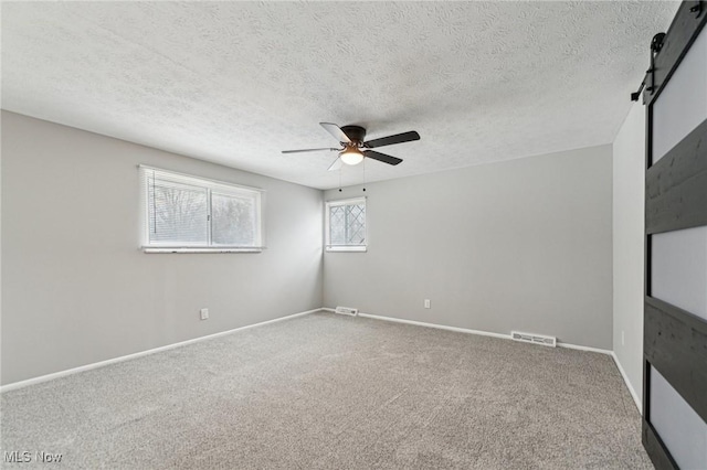 empty room with a barn door, carpet flooring, visible vents, baseboards, and a ceiling fan