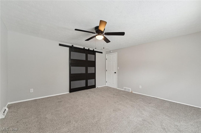 interior space with a textured ceiling, ceiling fan, a barn door, visible vents, and baseboards