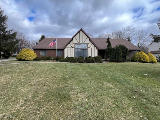 tudor-style house with a front lawn, a shingled roof, and brick siding