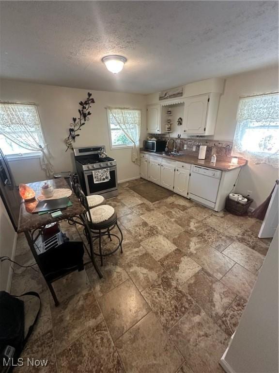 kitchen featuring stainless steel appliances, decorative backsplash, white cabinetry, a sink, and a textured ceiling