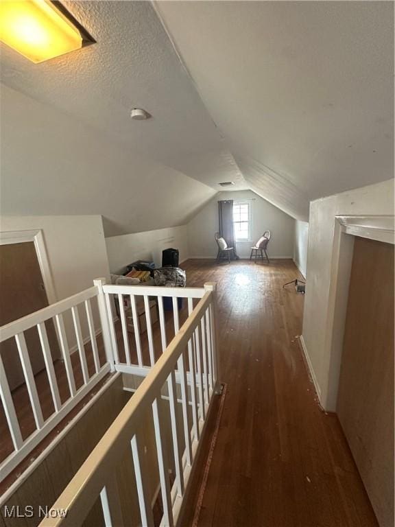 additional living space featuring wood-type flooring, vaulted ceiling, and a textured ceiling