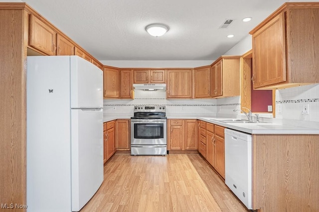 kitchen with white appliances, tasteful backsplash, light wood finished floors, under cabinet range hood, and a sink