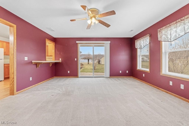 spare room with light carpet, ceiling fan, and baseboards