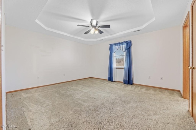 empty room featuring baseboards, visible vents, a ceiling fan, light colored carpet, and a tray ceiling