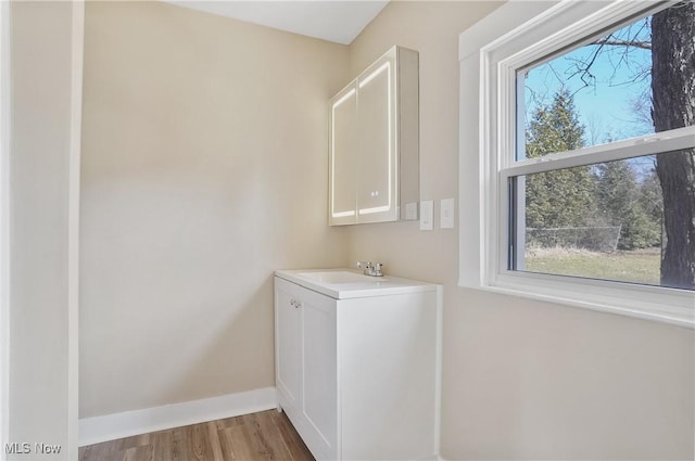 laundry area featuring wood finished floors, a sink, and baseboards