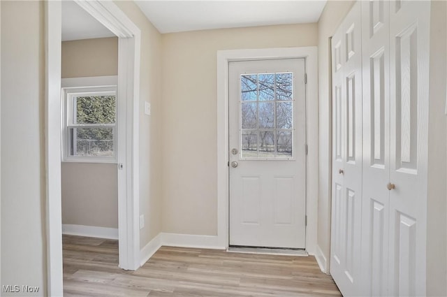 doorway featuring light wood-type flooring, a wealth of natural light, and baseboards