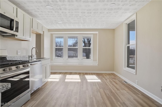 kitchen with baseboards, white cabinets, stainless steel appliances, light wood-type flooring, and a sink