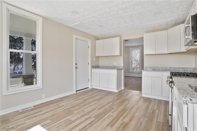 kitchen with light wood finished floors, visible vents, appliances with stainless steel finishes, a textured ceiling, and white cabinetry