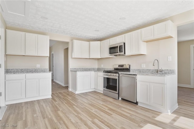 kitchen featuring light stone counters, stainless steel appliances, a sink, white cabinets, and light wood-type flooring