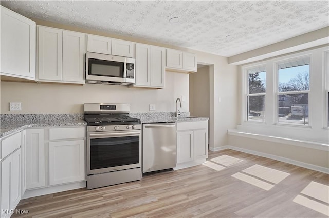 kitchen featuring light wood finished floors, appliances with stainless steel finishes, a sink, and white cabinets