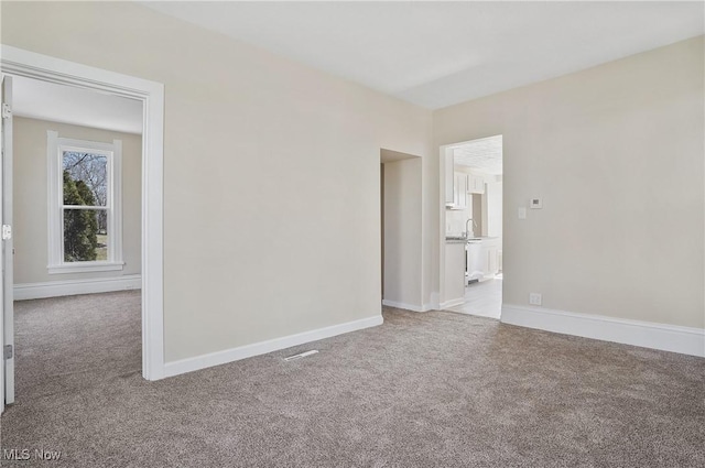 unfurnished room featuring carpet, a sink, and baseboards