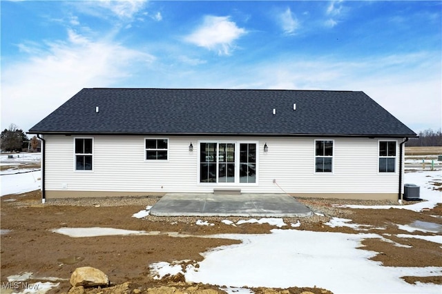 snow covered rear of property featuring a patio area, a shingled roof, and central AC unit