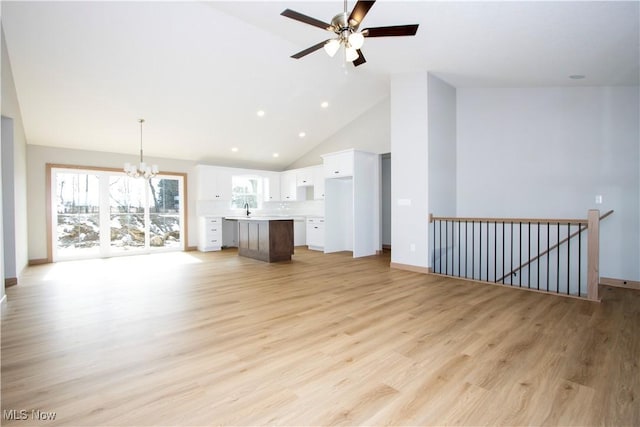 unfurnished living room with high vaulted ceiling, light wood-type flooring, a sink, and baseboards