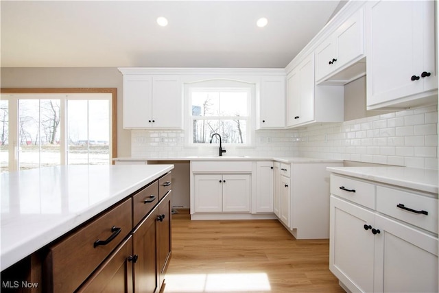 kitchen with light countertops, backsplash, light wood-style floors, white cabinets, and a sink