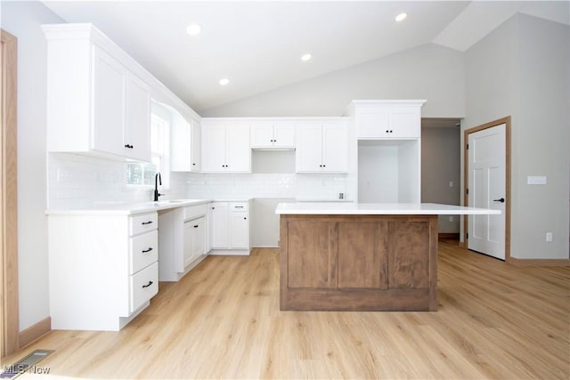 kitchen featuring light wood finished floors, tasteful backsplash, white cabinets, lofted ceiling, and a sink