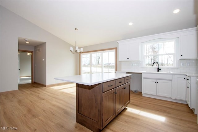 kitchen with a center island, light wood finished floors, stainless steel dishwasher, a sink, and vaulted ceiling