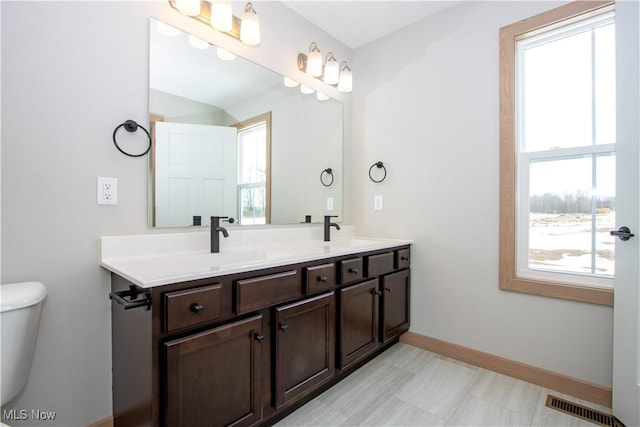 bathroom with double vanity, a sink, visible vents, and baseboards