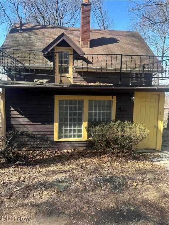 rear view of property featuring a chimney and a balcony