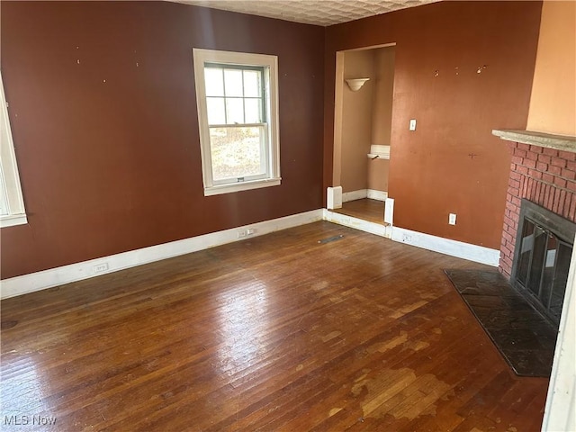 unfurnished living room with a brick fireplace, wood-type flooring, and baseboards