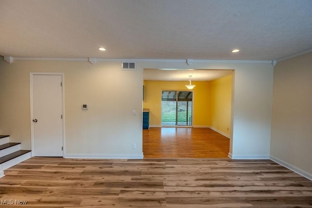 unfurnished room with a textured ceiling, wood finished floors, visible vents, and baseboards