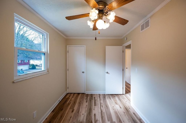 unfurnished bedroom with visible vents, ornamental molding, ceiling fan, wood finished floors, and baseboards