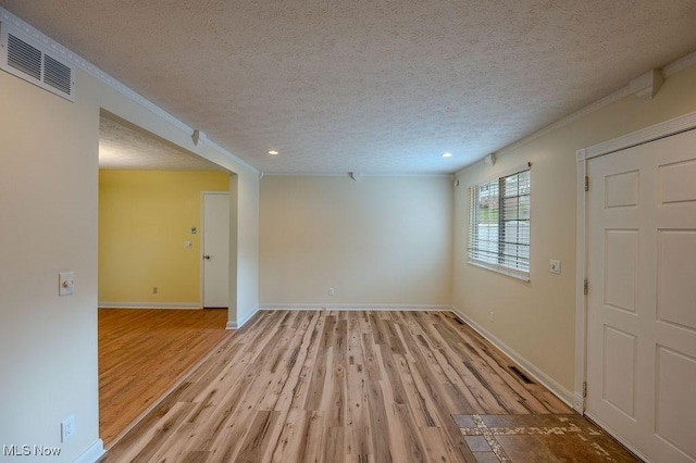 interior space featuring light wood-type flooring, visible vents, a textured ceiling, and ornamental molding