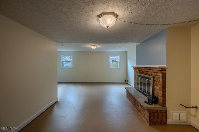 unfurnished living room featuring finished concrete flooring, visible vents, a brick fireplace, a textured ceiling, and baseboards