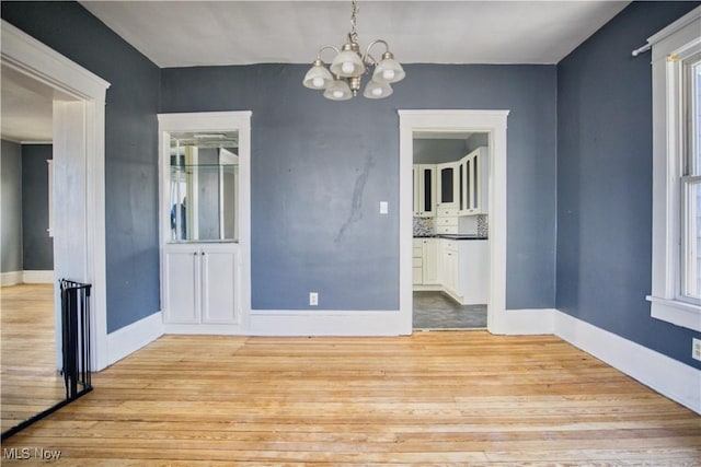 unfurnished dining area with light wood-type flooring, an inviting chandelier, and baseboards