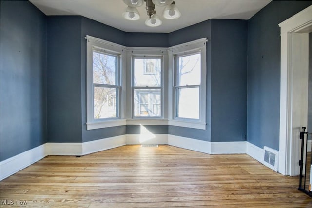 spare room featuring a chandelier, wood finished floors, visible vents, and baseboards