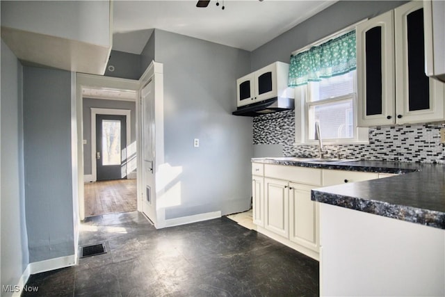 kitchen featuring dark countertops, baseboards, backsplash, and a sink