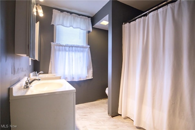 bathroom featuring double vanity, a sink, and toilet