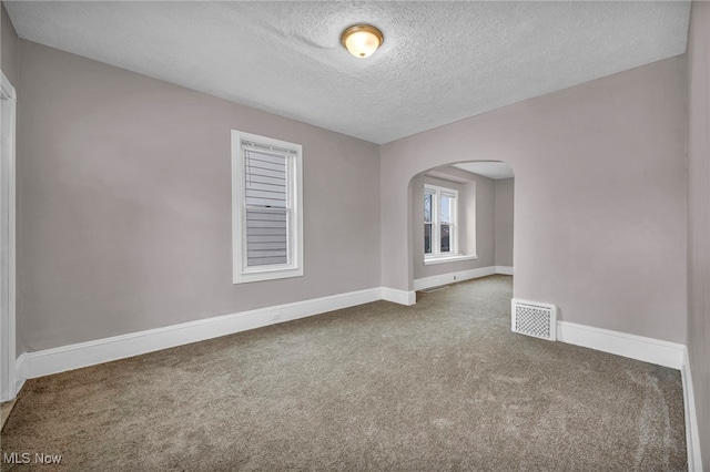 carpeted empty room featuring arched walkways, visible vents, a textured ceiling, and baseboards